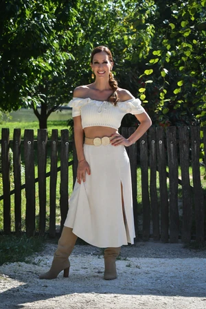 A törtfehér, vállra húzott crop top és a hozzá illő szoknya természetes, romantikus összhatást kelt Demcsák Zsuzsán, a széles öv és a velúrcsizma pedig rusztikus karaktert ad neki.